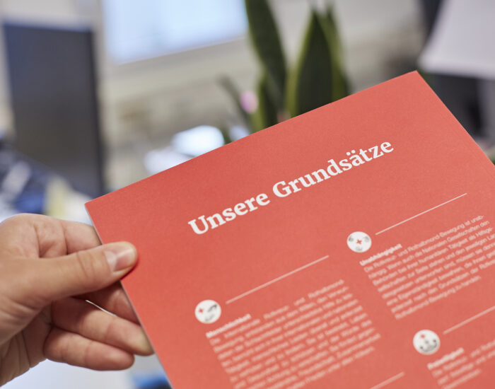 Ein rotes Papier, auf dem die Grundsätze des DRK abgebildet sind.