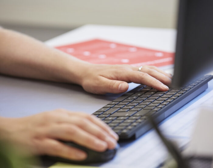 Nahaufnahme zweier Hände, die auf einer schwarzen Tastatur tippen.