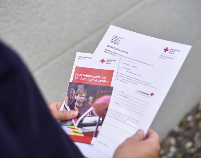 Zwei Hände halten einen Flyer zur Fördermitgliedschaft beim DRK in Bonn und eine Beitrittserklärung in der Hand.