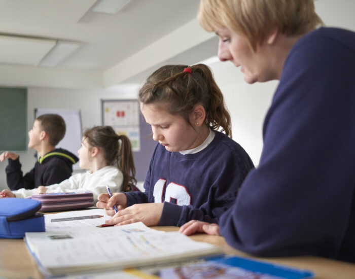 Eine Schulbegleiterin sitzt neben einem Schulkind und betreut sie bei dem Lösen von Schulaufgaben.