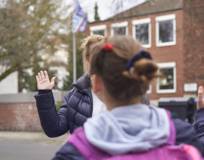 Eine Schulbegleiterin und ein Schulkind laufen aufeinander zu, im Begriff sich mit einem Handschlag zu begrüßen.