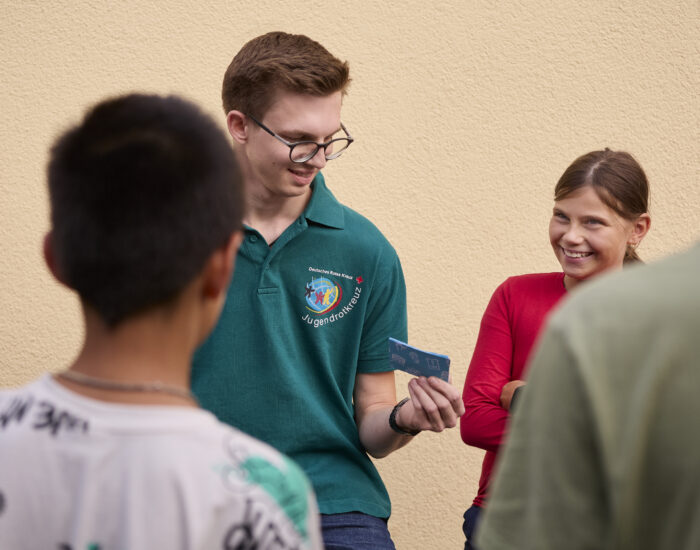 Ein Gruppenleiter des Jugendrotkreuzes hält Karten in der Hand, die er den Kindern zeigt. Sie lachen.