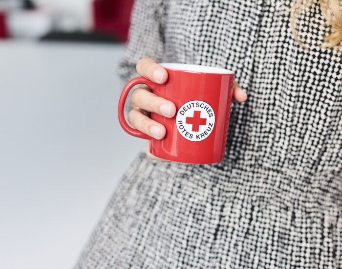 Eine Hand hält eine rote Tasse, auf der das Logo des Deutschen Roten Kreuzes zu sehen ist.