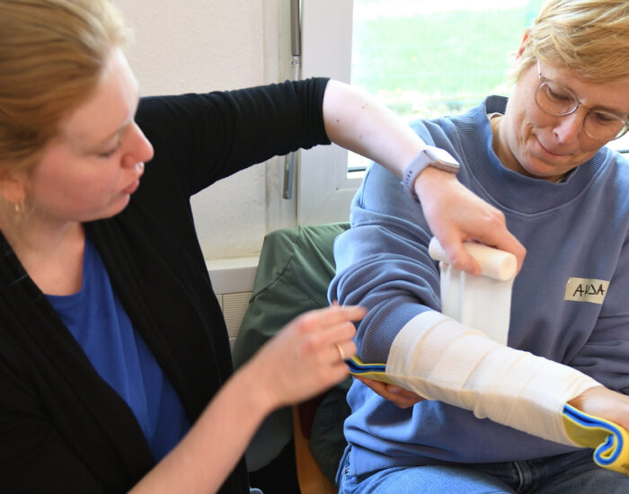 Zwei Personen üben das Anlegen einer Armschiene und eines Verbands.