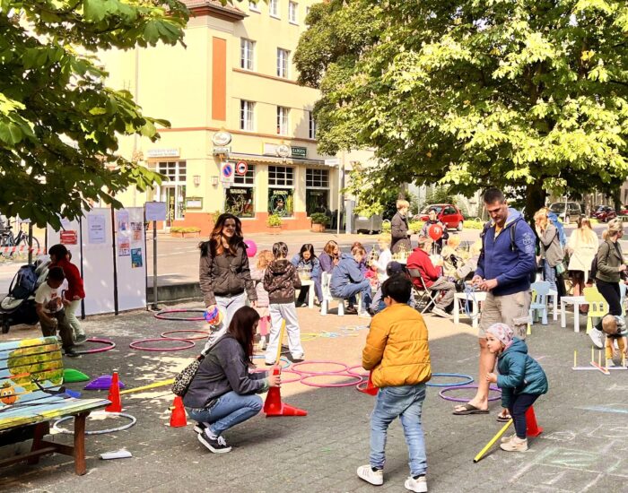 Kinder und ihre Eltern spielen mit Hoola-Hoop-Reifen und Kreide.