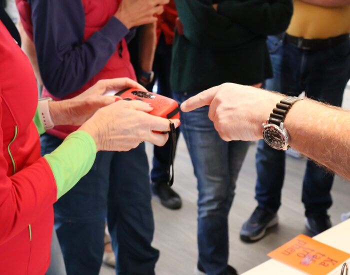 Eine Person hält ein Notfall-Kurbelradio in der Hand und eine anderen Person deutet mit dem Finger darauf.