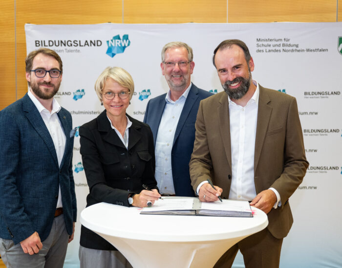 Vertreter verschiedener Organisation, worunter das Land NRW, stehen an einem Tisch und unterzeichnen die Kooperationsvereinbarung zur Laienreanimation an Schulen.