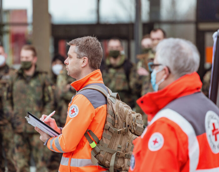 Zwei Personen vom DRK stehen vor einer Gruppe Menschen der Bundeswehr.