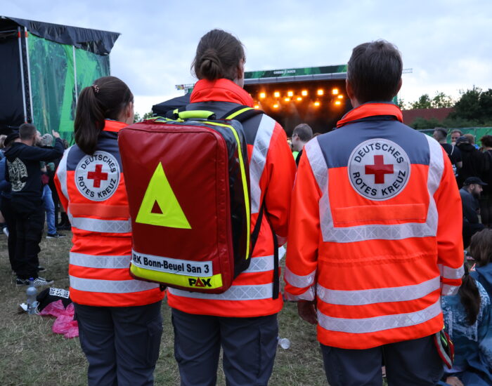 Drei Personen in DRK-Einsatzkleidung sind von hinten sehen. Die Person in der Mitte trägt einen Einsatzrucksack