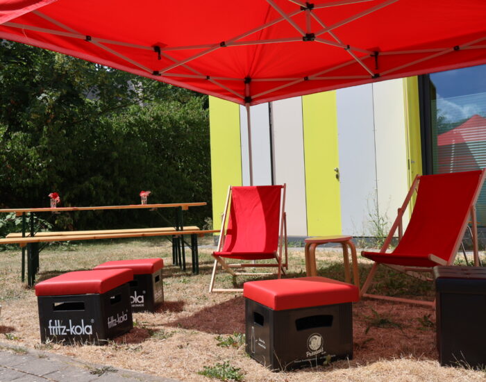 Ein roter Pavillon, zwei rote Liegestühle, eine Bierzeltgarnitur